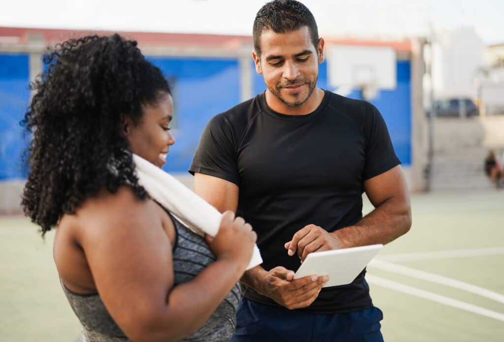 Woman talking with her personal trainer while checking a clipboard outdoors.