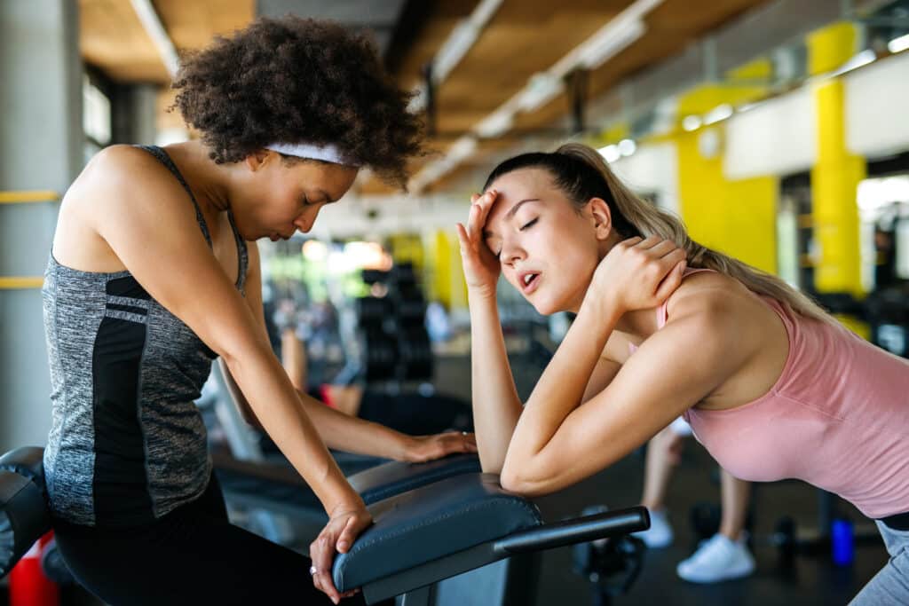 Two exhausted fitness female friends resting after working out at sports gym.