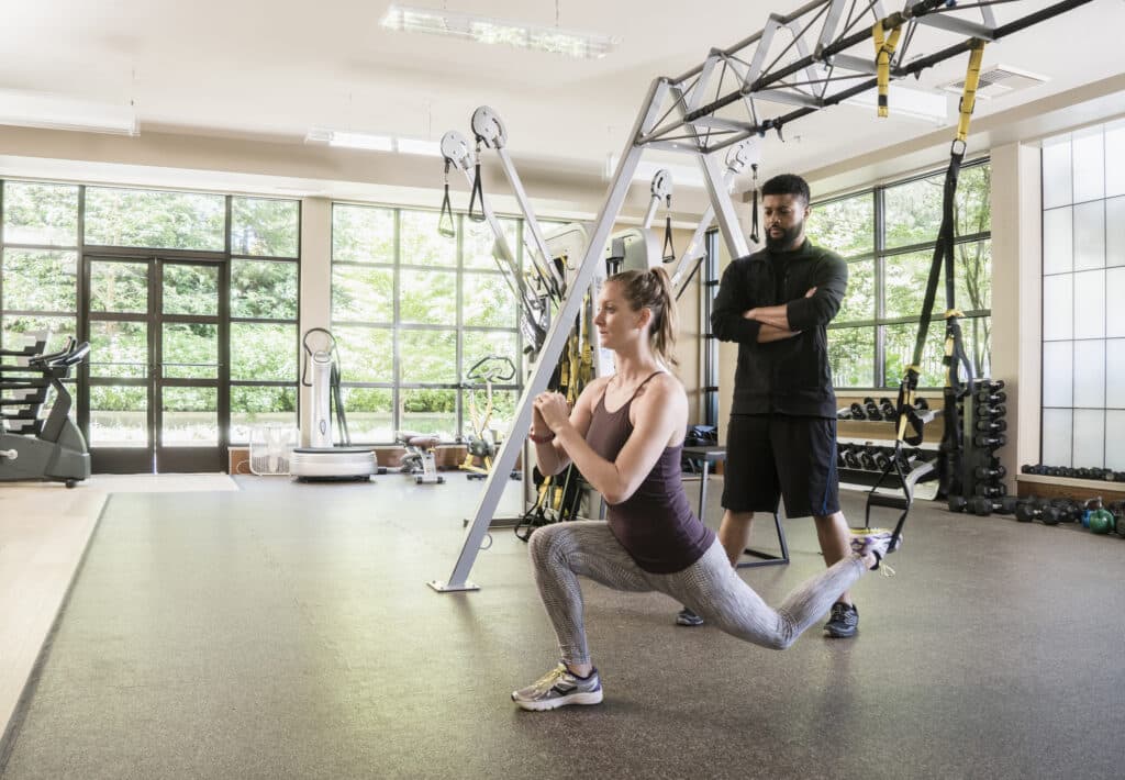 Fitness coach watching woman using exercise machine at gym.