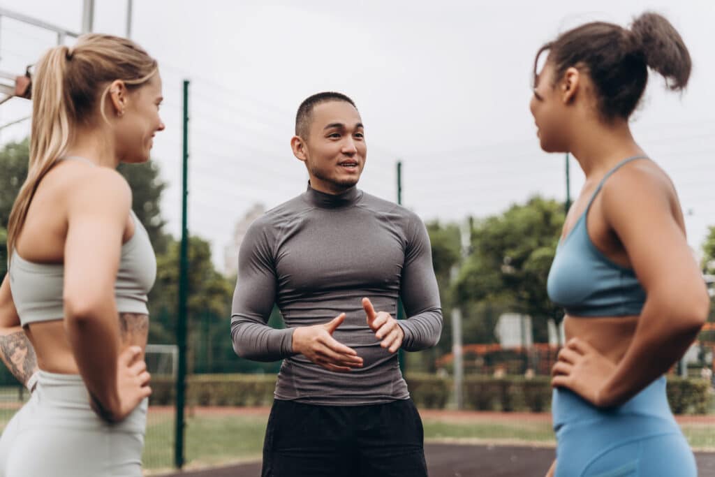 Group of happy, multinational women and man wearing stylish sportwear, talking, training together on the street, outdoors.