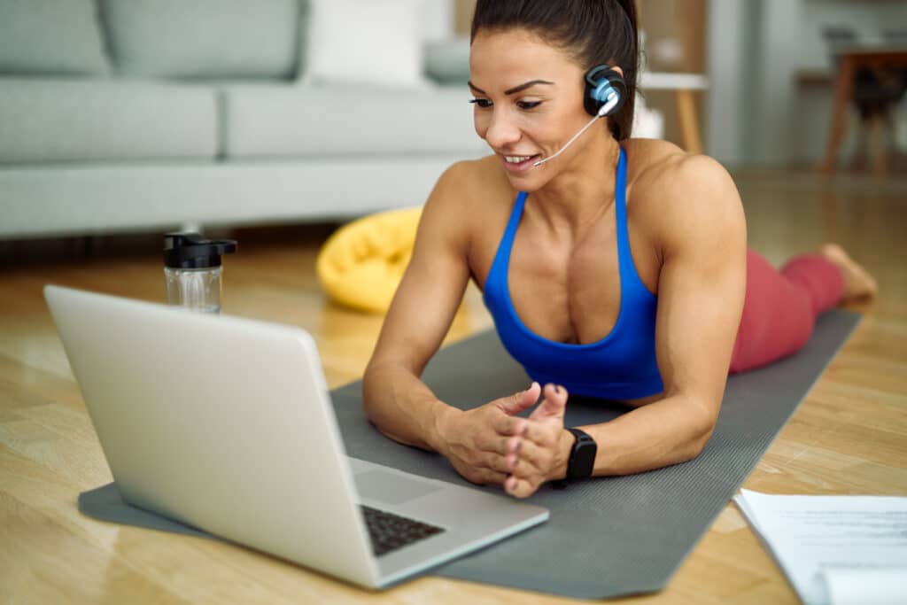 Happy athletic woman using laptop while having online exercise class at home.