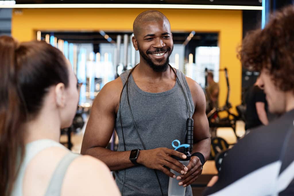 Personal trainer holding a tablet while discussing training progress with a senior male client wearing a yellow shirt outdoors.