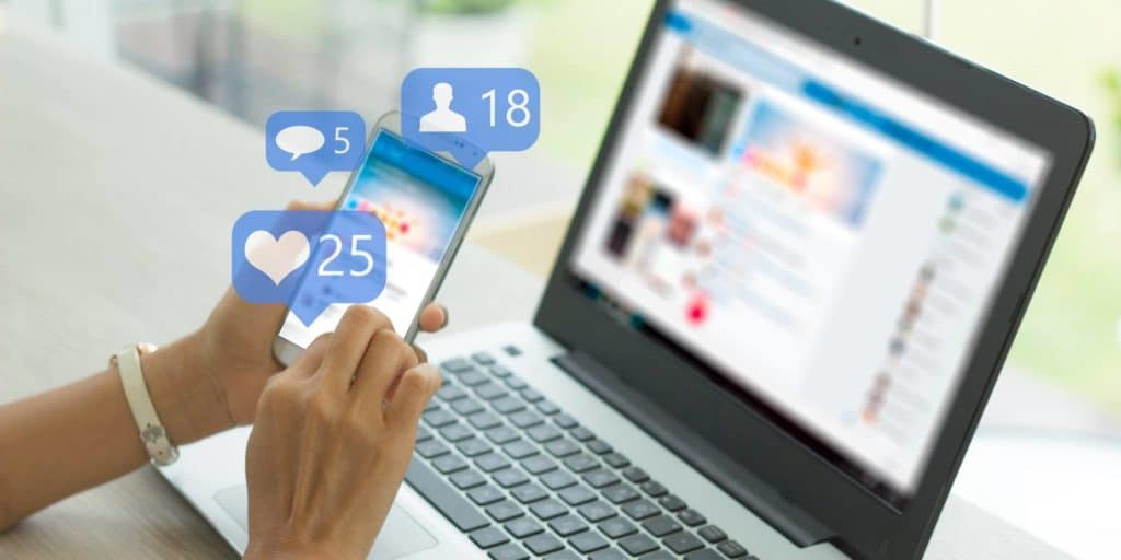 woman using social media on her phone and laptop with social media open in the background