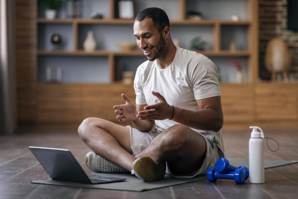 Smiling male online personal trainer conducting a session on his laptop while sat down.
