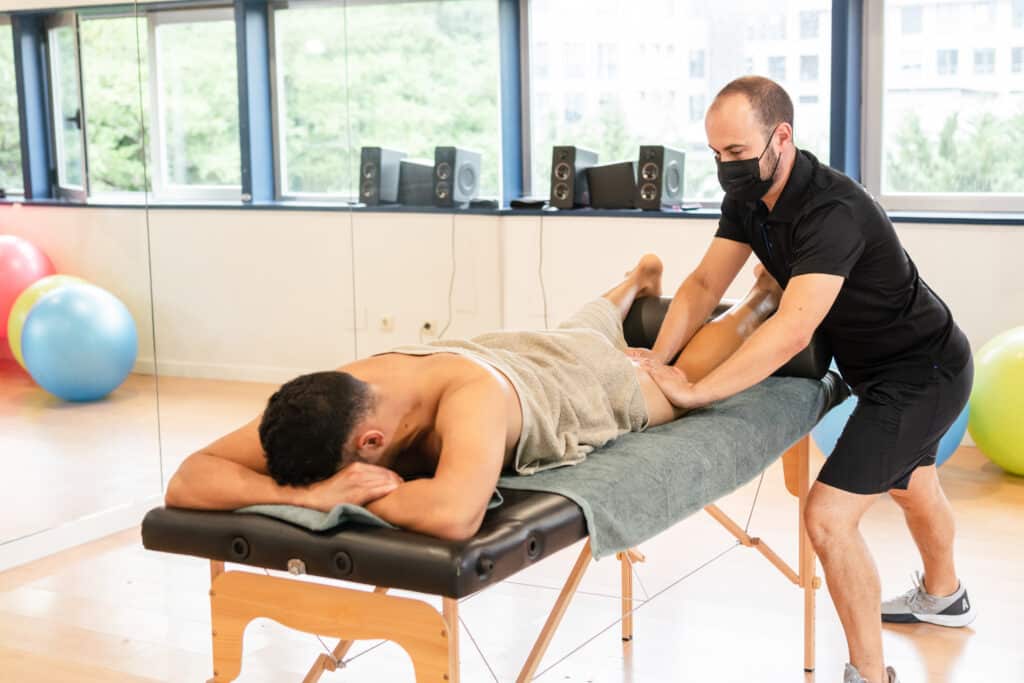A sporty man receiving a massage by a physiotherapist on a massage table.