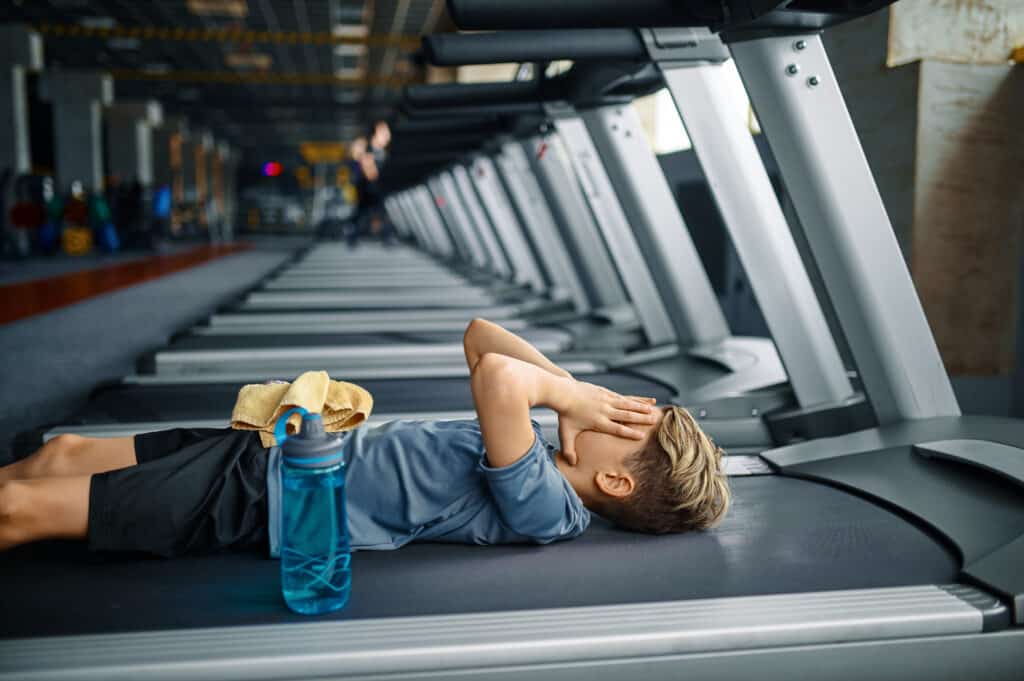 Tired young man lying on a treadmill in a gym.