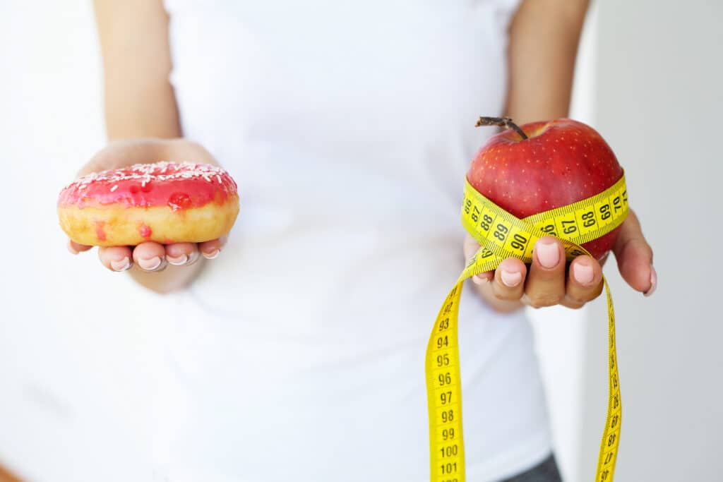 Woman holding a choice of harmful donut and fresh apple